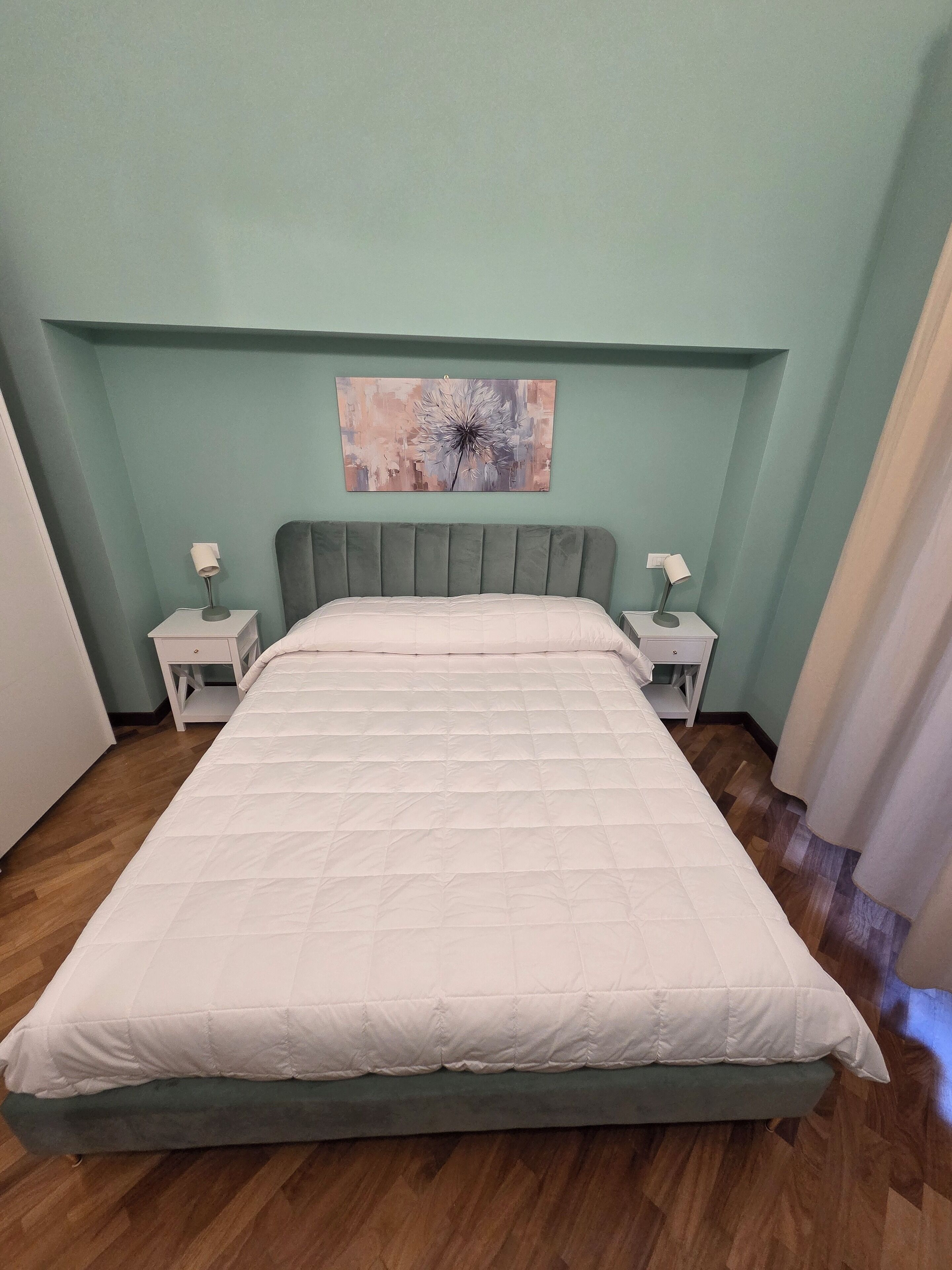 Ein Schlafzimmer mit einem großen Bett, zwei Nachttischen, einem Wandbild und einem Holzboden.