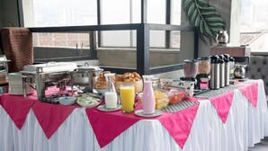 En morgenmadsbuffet med forskellige retter og drikkevarer, anrettet på et bord med hvid og lyserød dug.