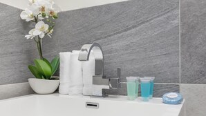 Kylpyhuone, jossa on valkoinen pesuallas, moderni hana, ruukussa oleva orkidea ja hygieniatuotteita.