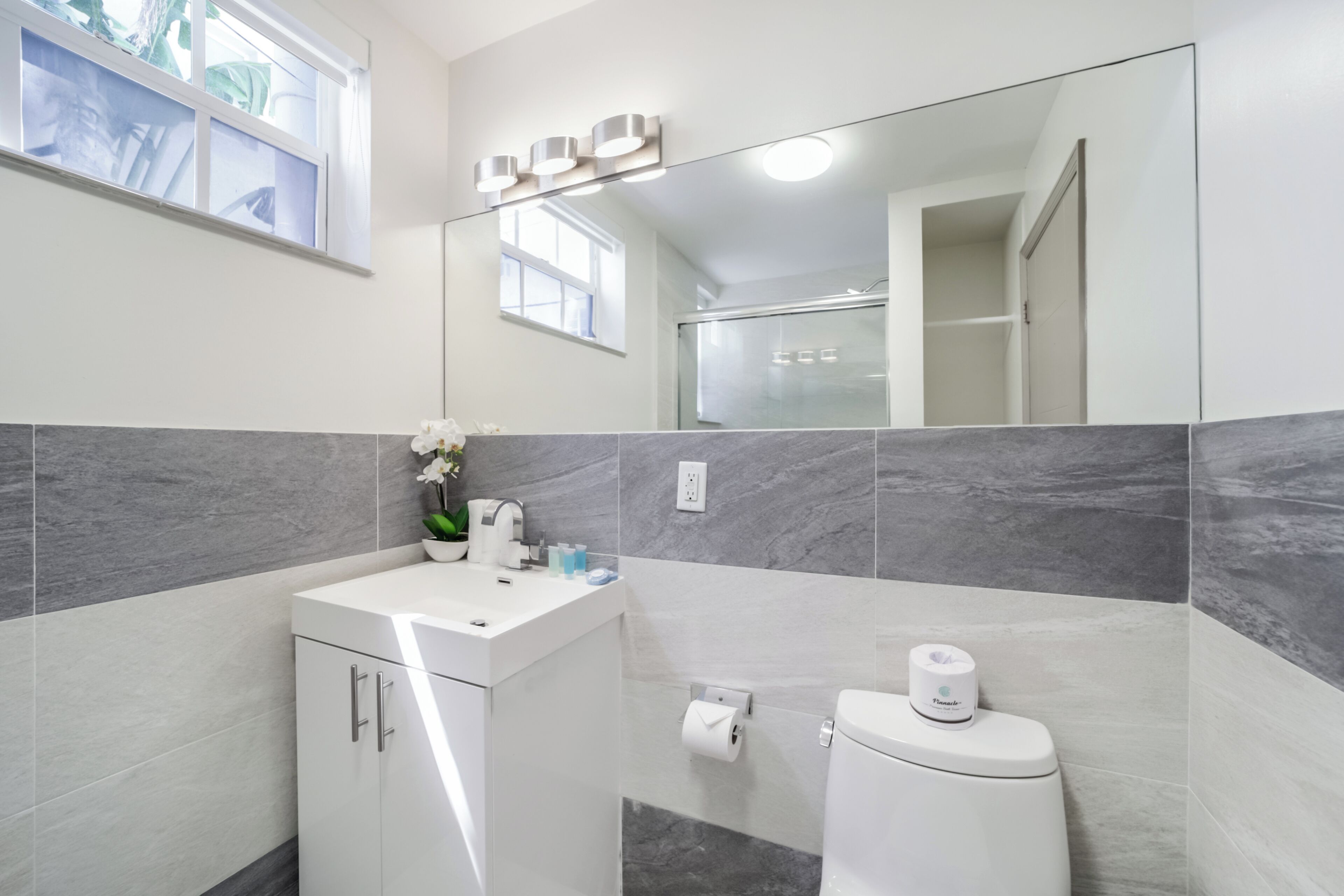 A modern bathroom with a white sink, a toilet, and a large mirror.