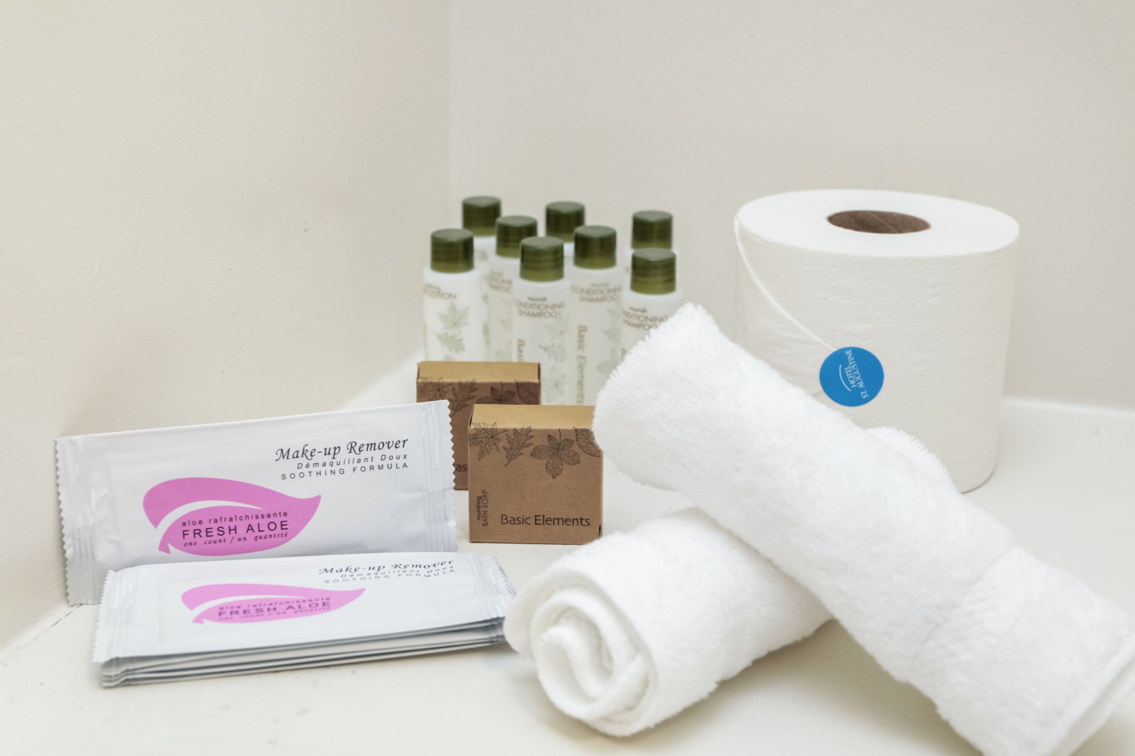 Un baño con una toalla blanca, un rollo de papel higiénico y varias botellas de champú y gel de baño.