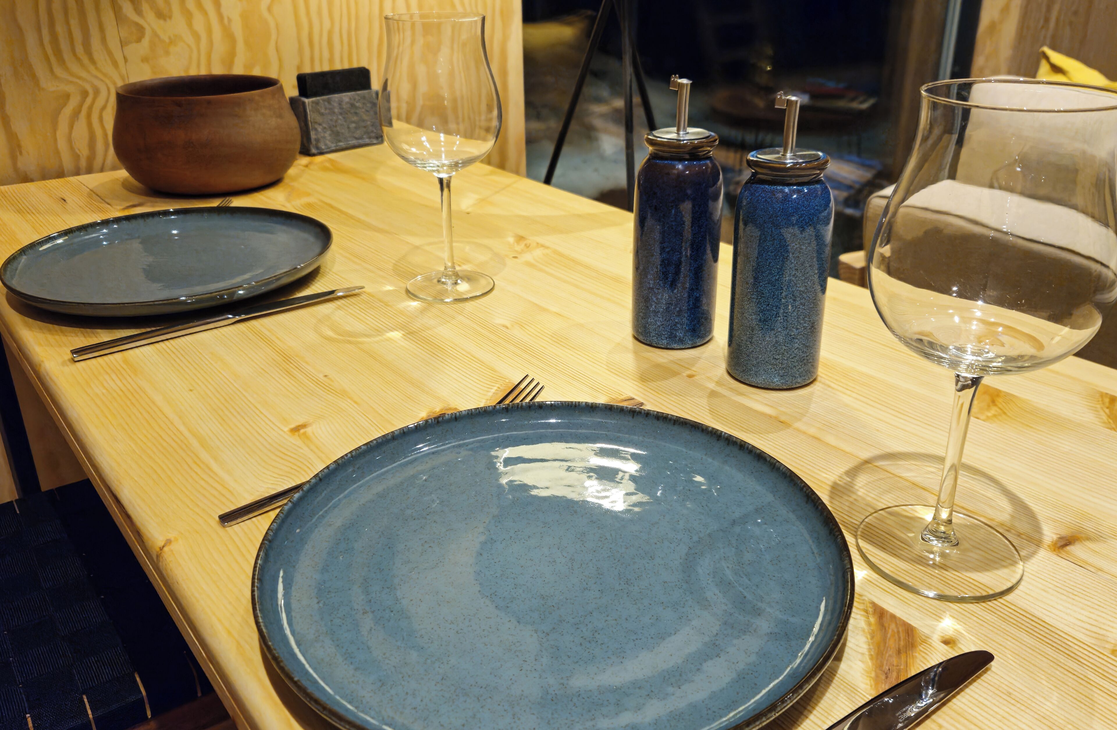 A wooden table with a blue plate, a wine glass, and a bowl.