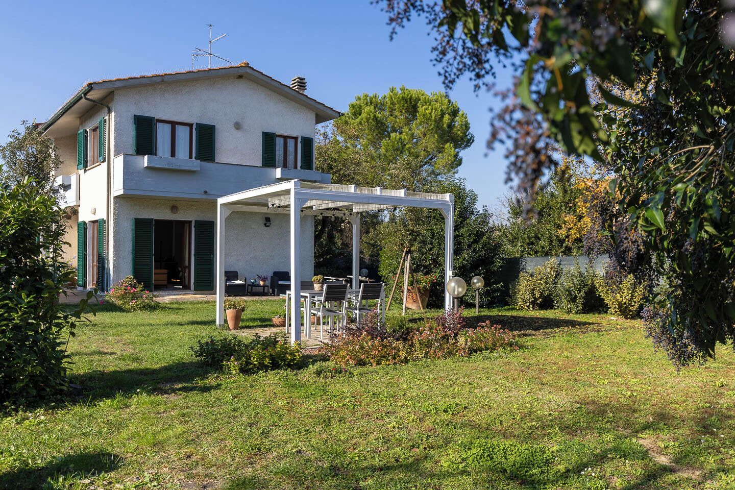 A two-story house with a covered patio area, a lawn, and surrounding greenery.