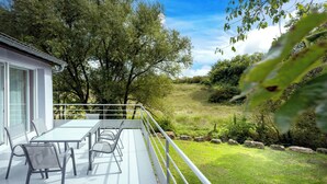 Eine Terrasse mit Tisch und Stühlen, mit Blick auf eine Rasenfläche mit Bäumen und einem Gebäude im Hintergrund.
