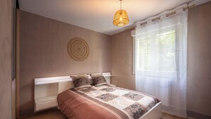 Ein Schlafzimmer mit Bett, Nachttischen, einer Wandleuchte und einem Fenster mit durchscheinenden Vorhängen.