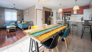 Ein modernes Wohnzimmer mit einem blauen Sofa, einem Holzesstisch mit Stühlen und einer Küchenzeile mit Bar.