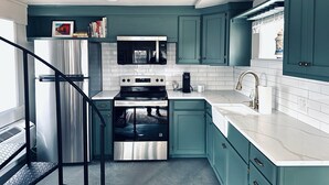 A modern kitchen with teal cabinetry, stainless steel appliances, and a white countertop. - Adorable 3 Bedroom/2 Bath Remodeled Cottage and Carriage House Built Circa 1930! (Glen Rose)