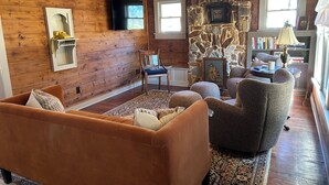 A cozy living room with wooden walls, a stone fireplace, a sofa, armchairs, and a bookshelf. - Adorable 3 Bedroom/2 Bath Remodeled Cottage and Carriage House Built Circa 1930! (Glen Rose)