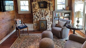 A cozy cabin interior with a stone fireplace, wooden walls, a bookshelf, and a comfortable seating area. - Adorable 3 Bedroom/2 Bath Remodeled Cottage and Carriage House Built Circa 1930! (Glen Rose)