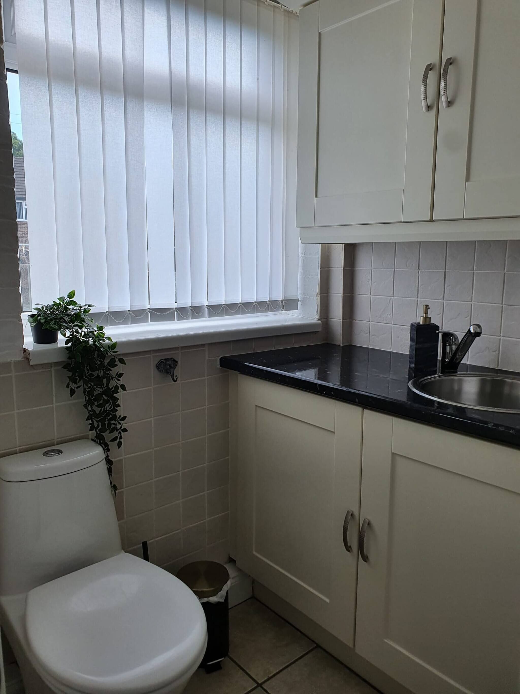 A small, clean kitchen with white cabinets, a black countertop, a sink, and a window with blinds.