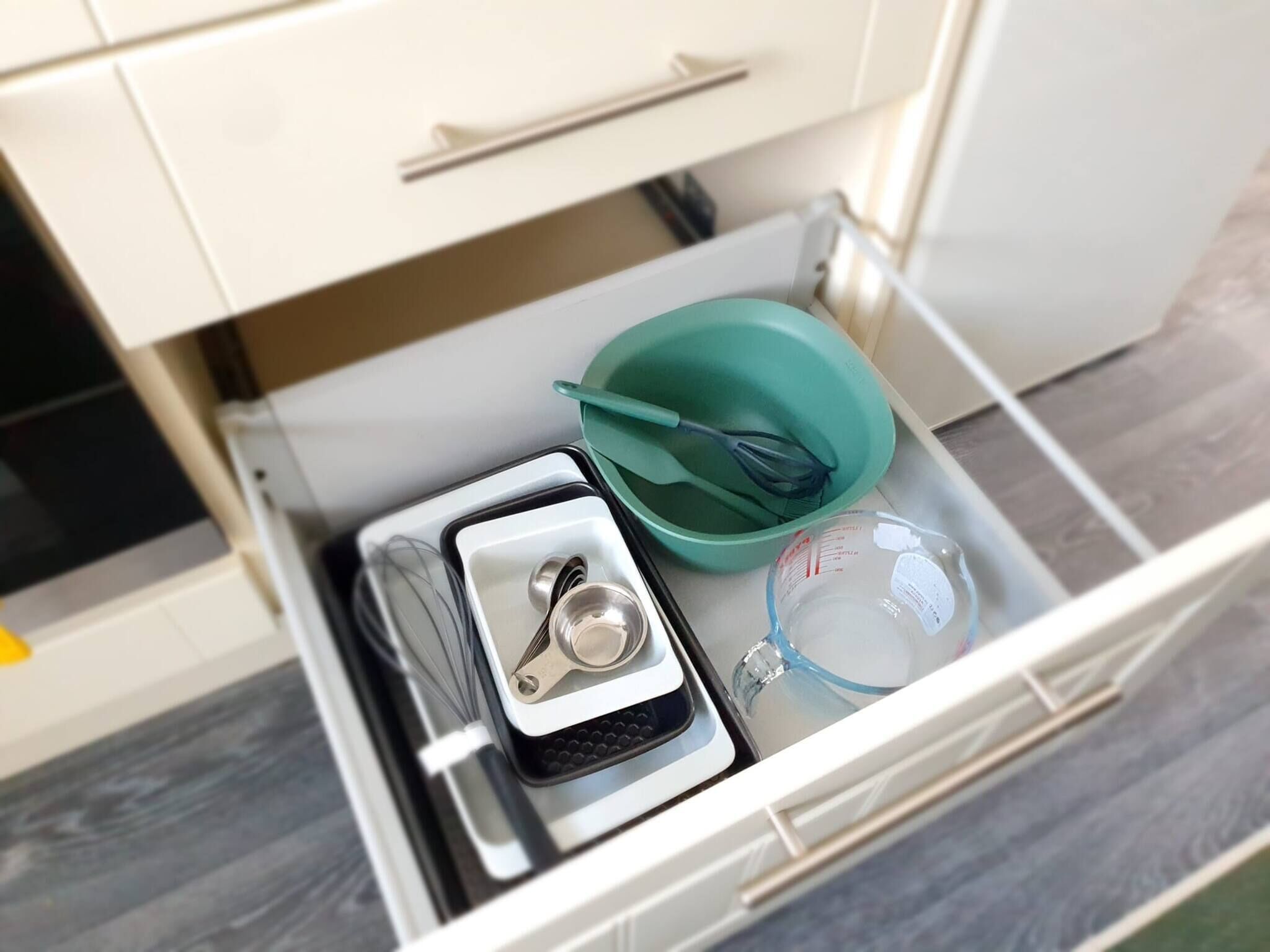 A kitchen drawer with a whisk, a measuring cup, and a green bowl.