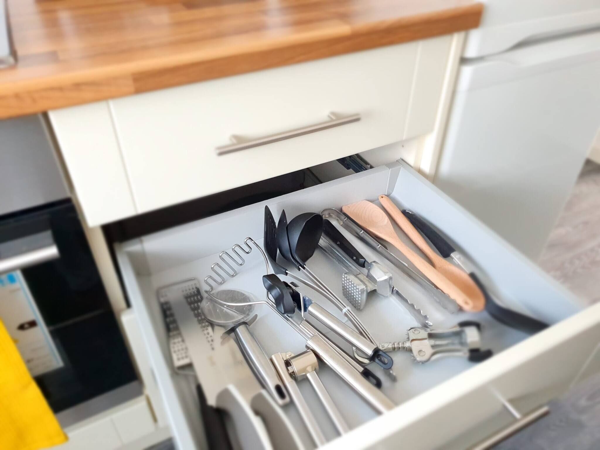 A drawer with various kitchen utensils including a grater, spatula, and tongs.