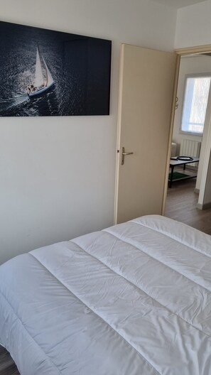 A bedroom with a bed, a door, and a painting of a sailboat on the wall. - Le Hublot de la Place (Saint-Hilaire-de-Riez)