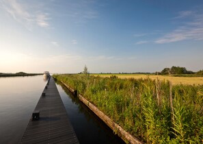 A wooden pier extending into calm water, surrounded by lush greenery and a clear sky. - Hublot de la Place - Downtown Sion, Beach Access (Saint-Hilaire-de-Riez)