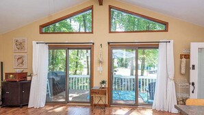 Een ruime kamer met houten vloeren, grote schuifdeuren naar een terras buiten, en een hoog plafond met dakramen.
