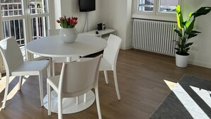 Een moderne, goed verlichte kamer met een ronde witte tafel en stoelen, een potplant en een radiator.