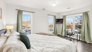 A hotel room with a large bed, a desk, and two windows with curtains.