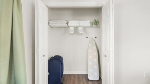 A small, neatly organized closet with shelves holding folded towels and an ironing board.