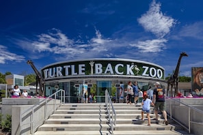 La entrada al zoológico Turtle Back bajo un cielo despejado, con visitantes entrando.