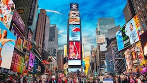 A busy urban street with tall buildings, large billboards, and a crowd of people.