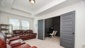 Una sala de estar con un sofá de cuero marrón, un televisor y una puerta que da a otra habitación.