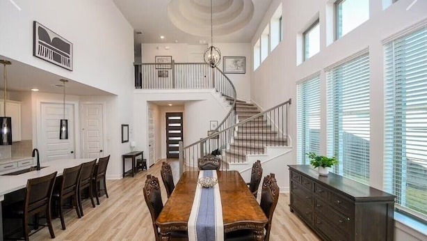 Un comedor amplio con techo alto, una escalera que sube a un nivel superior y ventanas grandes con persianas.