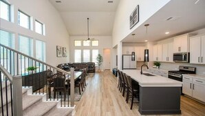 Una cocina amplia con una isla central, electrodomésticos modernos y un comedor con una escalera que sube a un nivel superior.