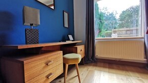 A room with a wooden desk, a chair, a lamp, a mirror, and a window with a view of greenery. - Comfortable gîte in the heart of the Cotentin region, ideal for families (La Hague)