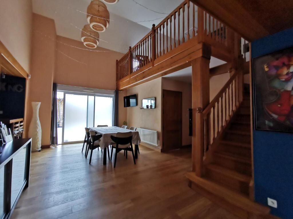 Une pièce spacieuse avec un escalier en bois, un coin repas comprenant une table et des chaises, et une grande fenêtre laissant entrer la lumière naturelle.
