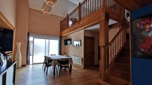 A spacious room with a wooden staircase, a dining area with a table and chairs, and a large window providing natural light. - Comfortable gîte in the heart of the Cotentin region, ideal for families (La Hague)
