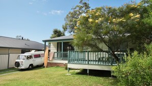 A house with a covered porch, a car parked in the driveway, and a tree with yellow flowers.