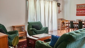 A living room with green armchairs, a wooden coffee table, a wicker side table, and a dining area with wooden chairs and a table.