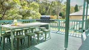 An outdoor deck with a table and chairs, a grill, and a view of trees and a house.