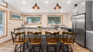 A modern kitchen with a central island, stainless steel appliances, and a dining area with forest-themed chairs. - The Pine Getaway on 60 Acres with Hot Tub (Pine)