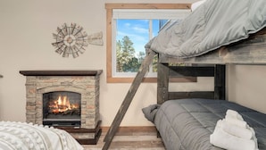 A cozy room with a stone fireplace, a window with a view of trees, and a bunk bed. - The Pine Getaway on 60 Acres with Hot Tub (Pine)