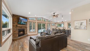 A spacious living room with a stone fireplace, a large leather sofa, and a television mounted on the wall. - The Pine Getaway on 60 Acres with Hot Tub (Pine)