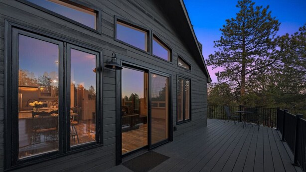 A modern house with large sliding glass doors, a deck, and a view of the outdoors. - The Pine Getaway on 60 Acres with Hot Tub (Pine)