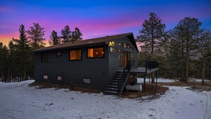 A two-story cabin with a deck, surrounded by trees and snow. - The Pine Getaway on 60 Acres with Hot Tub (Pine)