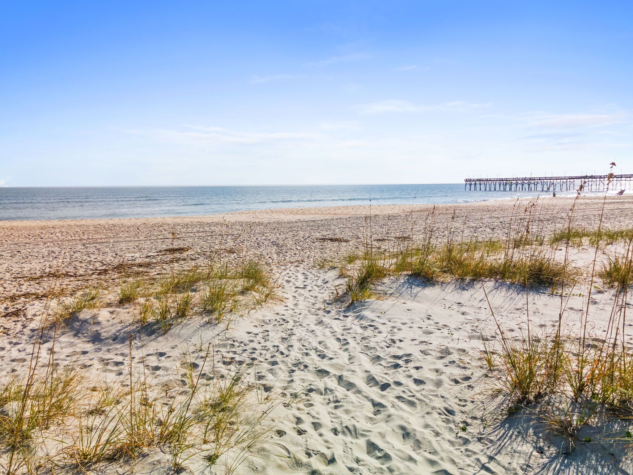 A beach with sand dunes and a pier in the background.