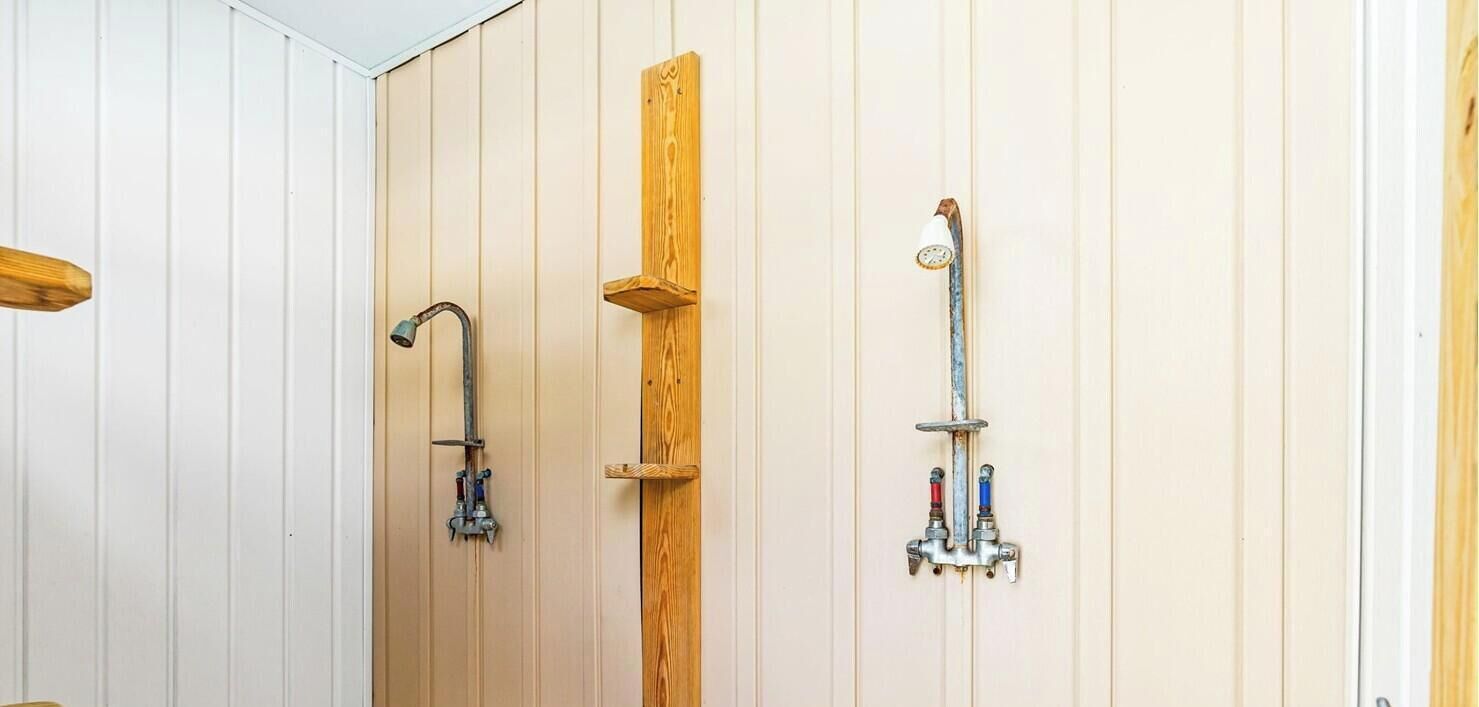 A shower with a wooden panel wall, a handheld showerhead, and a wall-mounted faucet.