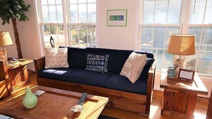A cozy living room with a dark blue sofa, wooden coffee table, and a view of the outdoors through large windows. - 5 Bedroom Quiet Neighborhood Short Walk to Beach (Ocean Isle Beach)