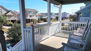 A covered porch with white railings, wooden deck, and several chairs. - 5 Bedroom Quiet Neighborhood Short Walk to Beach (Ocean Isle Beach)