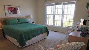 A bedroom with a large bed, a desk with a lamp, wicker chairs, and a window with a view. - 5 Bedroom Quiet Neighborhood Short Walk to Beach (Ocean Isle Beach)