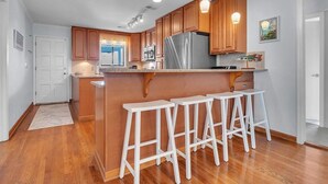 Eine moderne Küche mit Holzausstattung, einem Edelstahlkühlschrank und einer Bar mit weißen Hockern.