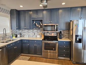 A modern kitchen with dark blue cabinets, stainless steel appliances, and a tiled backsplash. - 4 Bedroom Oceanfront Spacious Beach House (Ocean Isle Beach)