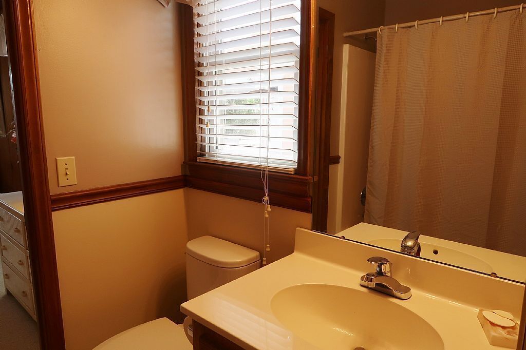 Une salle de bain avec des toilettes, un lavabo et une fenêtre avec des stores.
