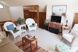 A cozy living room with wicker furniture, a television, and a painting of birds. - 4 Bedroom Third Row Cozy Beach Cottage (Ocean Isle Beach)