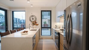 A modern kitchen with a central island, stainless steel appliances, and large windows offering views of the city. - The Big Lohbow-Ski Haus (Revelstoke)