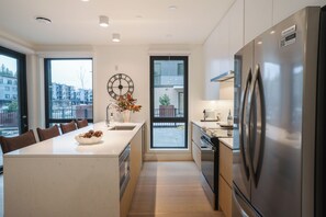 A modern kitchen with a central island, stainless steel appliances, and large windows offering views of the city. - The Big Lohbow-Ski Haus (Revelstoke)