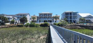 A beachfront hotel with multiple-story buildings, a wooden boardwalk, and a clear blue sky. - Large Luxury Property on Marsh Private Pool Hot Tub (Ocean Isle Beach)